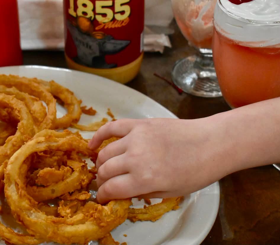 Onion rings on a plate beside a bottle of the Anvil's own 1855 Sauce